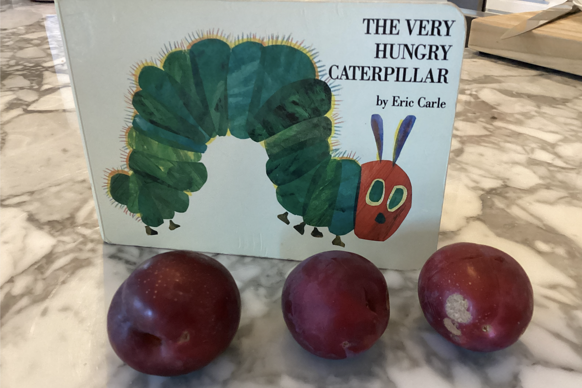 Cover of The Very Hungry Caterpillar with 3 plums in front of it.